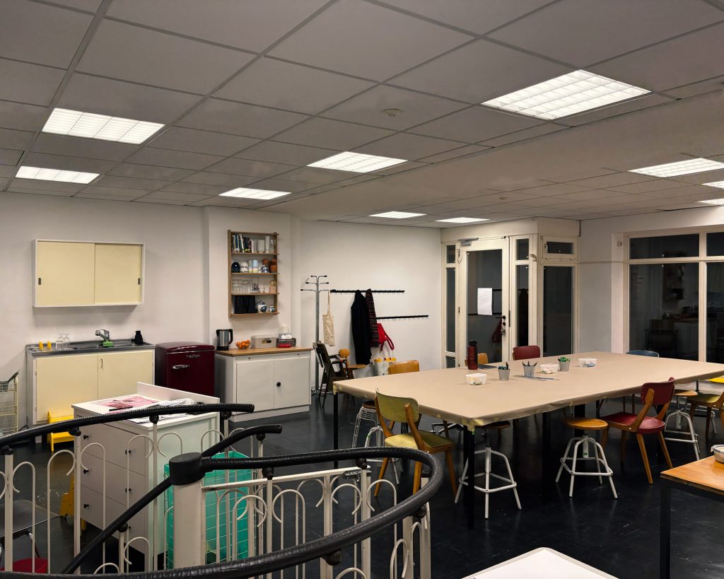 Aufnahme des Kreativraums mit Eingangsbereich, großem Tisch zum Arbeiten und bunten Bildern an den Wänden.